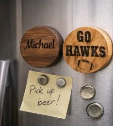 Wooden magnets with 'Michael' and 'GO HAWKS' text on a metallic surface with a bottle cap and note.