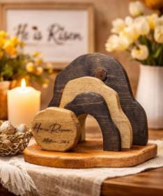 Decorative wooden arch with 'He is Risen' inscription on a table with candles and flowers.